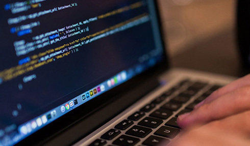 Code shown on laptop screen with fingers typing on keyboard