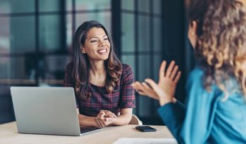 Two women talking next to a laptop/