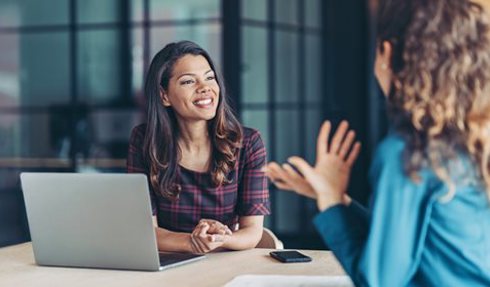 Two women talking next to a laptop/