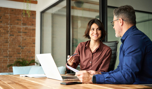 Woman talking to a man while working on a laptop